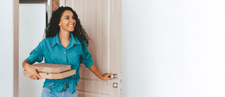 Woman With Curly Hair Smiles While Delivering Pizza to a Home Entranceの写真素材
