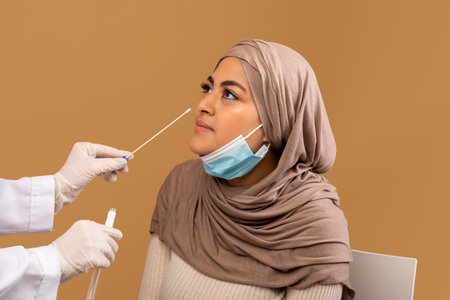 Coronavirus diagnostic. Nurse making covid-19 PCR test for arab lady using sterile swab stick, brown backgroundの写真素材