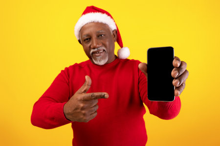 Cheerful Senior Man in Santa Hat Shows Blank Smartphone Screen for Christmas Promotionの写真素材