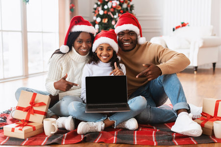 Happy Black Family Celebrating Christmas and Showing Blank Screen on Laptop for Festive Offersの写真素材