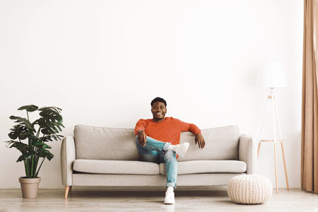 Comfortable Young Man Relaxing on a Light Gray Sofa in a Modern Living Roomの写真素材