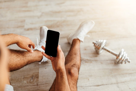Man Resting on the Floor After Workout, Checking Phone While Exercising in Gymの写真素材