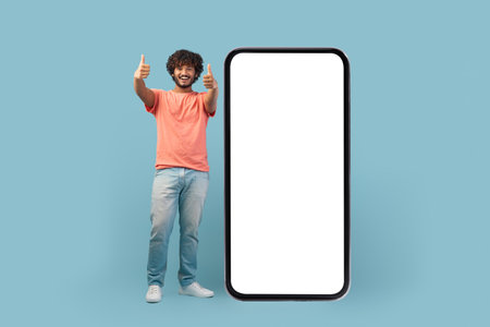 Happy Eastern Man Shows Big Mobile Phone With Blank Screen, Ready for App Recommendationの写真素材