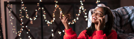 Girl Enjoying a Cozy Phone Call With Holiday Lights Glowing in the Backgroundの写真素材