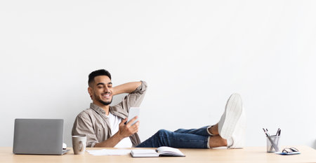Man Relaxing at Home Office With Feet on Table Using Mobile Phone for a Break During Work Hoursの写真素材