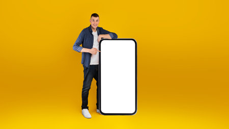 Person Standing Next to a Large Blank Phone Display, Smiling in Front of a Bright Yellow Background