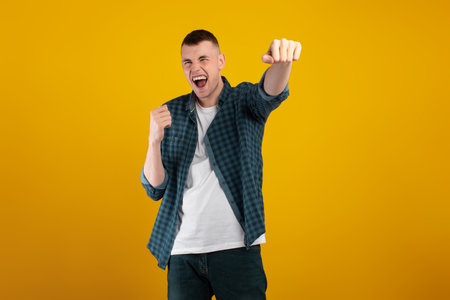 Young Man Celebrates With Joy and Enthusiasm Against a Bright Yellow Background in a Casual Outfitの写真素材