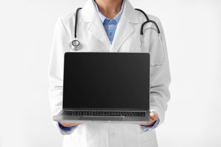 Young Indian Female Doctor Holds Computer for Telemedicine Consultation on White Backgroundの写真素材