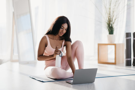 Young Black Woman Engaged in Online Workout Session at Home During Lockdownの写真素材