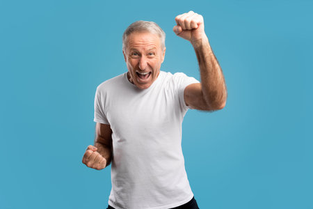 Excited Senior Man Celebrating Success With Joyful Gestures on Blue Backgroundの写真素材