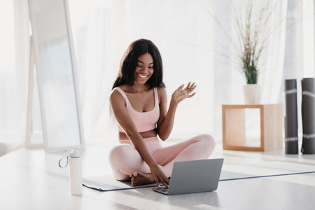 Young African American Woman Greets Online Trainer While Practicing Yoga at Homeの写真素材