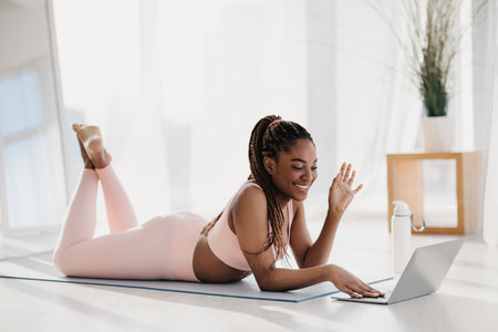 Young Woman Greets Personal Trainer Online for Home Workout Session on Yoga Matの写真素材