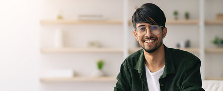 Young Man With Glasses Smiling Indoors in a Modern, Bright Settingの写真素材