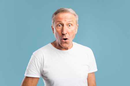 Mature Man Expresses Surprise in Studio Setting With Blue Backgroundの写真素材