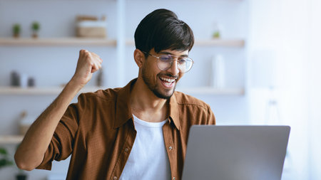 Man Celebrating Success While Using Laptop Indoors During Daytimeの写真素材