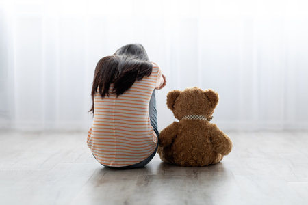 Young Girl Sitting on Floor With Teddy Bear, Sharing a Quiet Moment Together in a Sunlit Roomの写真素材