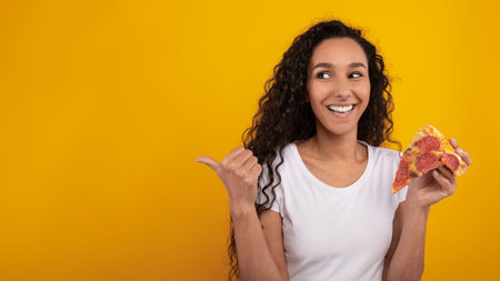 Excited Young Woman Enjoys Slice of Pizza While Pointing at Empty Space for Advertisementの写真素材