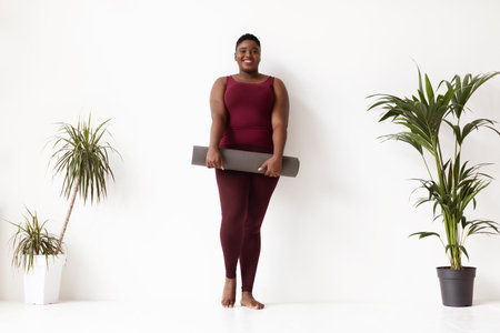 Cheerful Young Woman Poses With Fitness Mat in Yoga Studio Surrounded by Plantsの写真素材