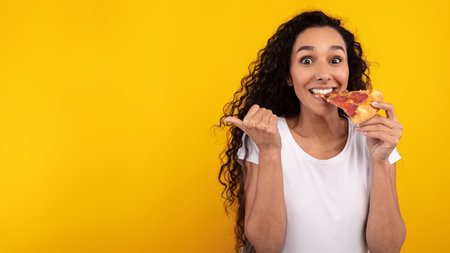Happy Lady Enjoys Slice of Pizza While Smiling and Pointing at Blank Space in Bright Settingの写真素材