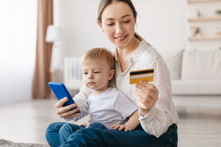Mother and Child Engaging in Online Shopping With a Smartphone and Credit Card at Homeの写真素材