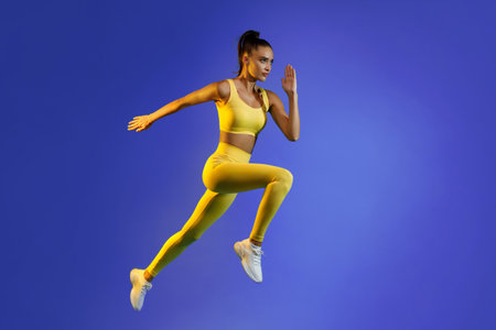 Woman in Yellow Activewear Performing a Dynamic Leap Against a Blue Backgroundの写真素材