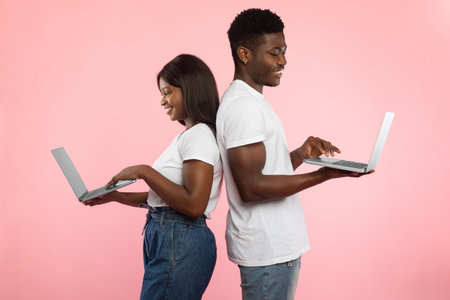 Cheerful African American Couple Enjoying Technology Together in Pink Studio Settingの写真素材