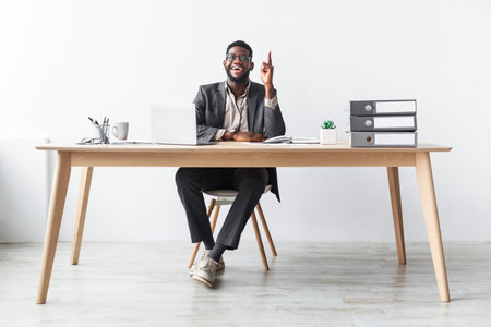 African American Office Worker Celebrates Innovative Idea While Sitting at Desk in Officeの写真素材