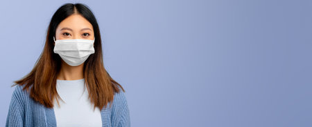 Young Woman Wearing a Mask Poses Against a Simple Blue Background During a Health Campaignの写真素材