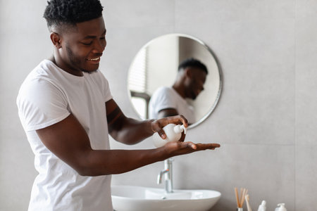 African Man Applying Liquid Soap While Washing Hands in Bathroom at Home During Daytimeの写真素材