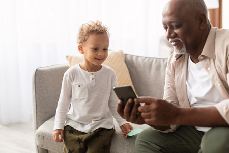 Happy Grandpa Teaching Grandson How to Use Smartphone at Home