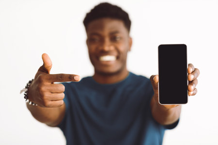 Man Smiles and Shows Smartphone Against a Plain Background in Modern Settingの写真素材