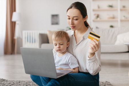 Mother Shopping Online With Toddler at Home Using Laptop and Credit Cardの写真素材