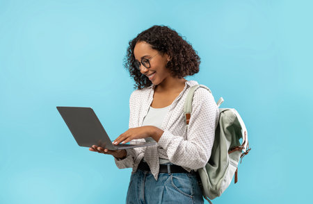 Happy Young African American Female Student Using Laptop for Online Learning Against Blue Backgroundの写真素材