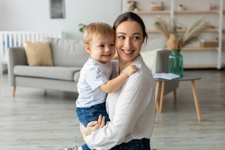 Mother Holds Smiling Child in Modern Living Room With Cozy Decor and Natural Light During Afternoon Playtimeの写真素材