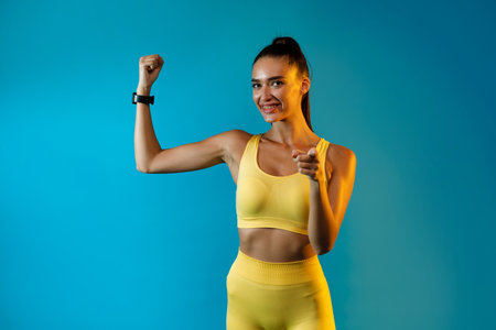Fitness Lady Shows Biceps While Pointing at Camera Against a Blue Backgroundの写真素材