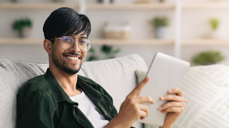 Young Man Enjoys Reading on a Tablet While Sitting Comfortably at Homeの写真素材
