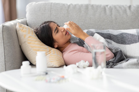 Millennial Indian Woman Recovering From Flu While Resting on Sofa With Medications and Waterの写真素材
