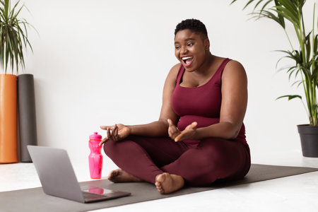 Overweight African American Woman Enjoys Video Chat With Yoga Coach on Fitness Matの写真素材
