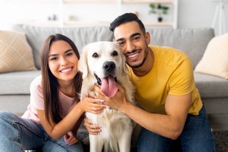 Couple Smiles While Posing With Their Golden Retriever at Home on a Cozy Sofa in the Living Roomの写真素材
