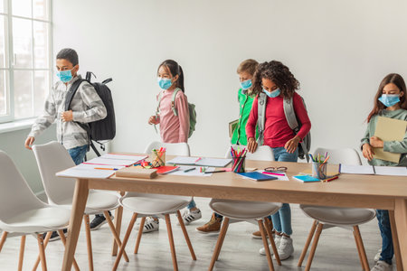 Diverse School Kids With Backpacks and Face Masks Entering a Modern Classroom During a Pandemicの写真素材