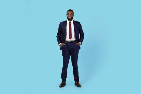 Portrait Of Handsome Young Black Businessman In Suit Standing On Blue Backgroundの写真素材