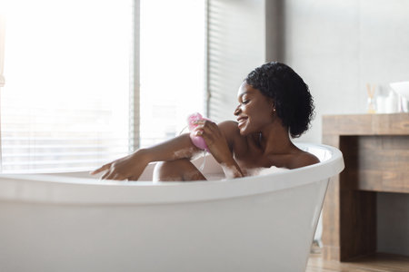 Relaxed African American Woman Enjoying a Soothing Bath at Home in a Beautiful Bathtubの写真素材