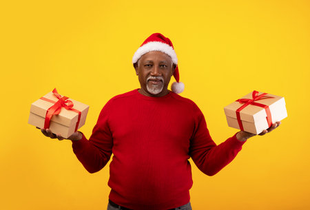 Senior Black Man in Santa Hat Holds Christmas Gifts Against Bright Orange Backgroundの写真素材