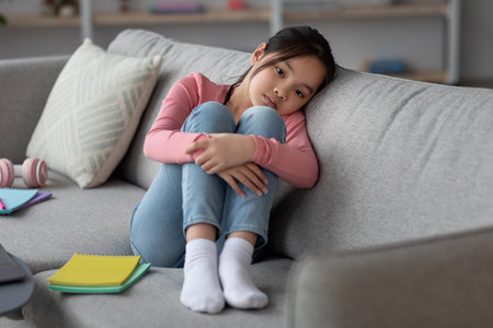 Young Girl Sitting on a Sofa, Appearing Thoughtful and Contemplative in a Cozy Living Room Settingの写真素材