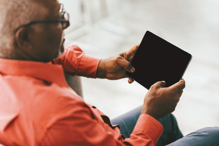 Senior Man Using a Tablet While Sitting Comfortably in a Modern Living Roomの写真素材