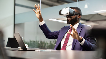 Excited black businessman sitting at workdesk, using VR glassesの写真素材