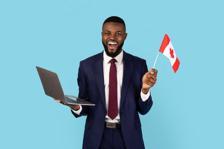 Excited Black Businessman With Canadian Flag And Laptop Posing Over Blue Backgroundの写真素材