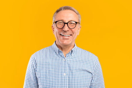 Mature Man Smiling in Glasses Poses at Studio With Bright Yellow Background