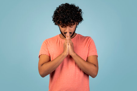 Eastern Young Man Praying for Help and Support Against a Blue Backgroundの写真素材