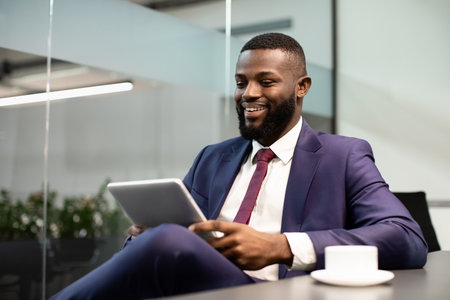 Cheerful black businessman using digital tablet at office, copy spaceの写真素材